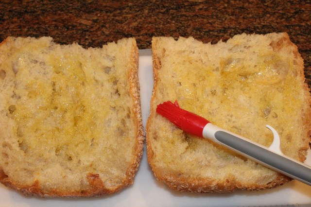 Brush sesame Italian loaf with olive oil for Kel's muffulettas